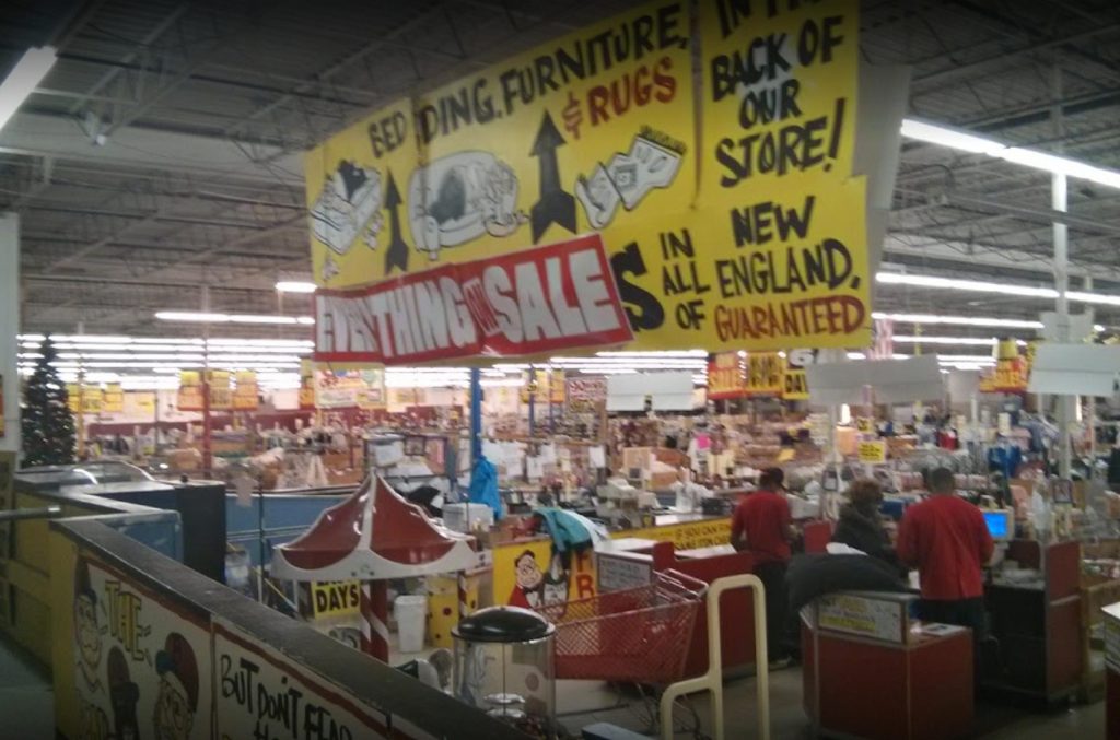 Interior view of a Building 19 store, showcasing colorful sale signs and a busy shopping environment.