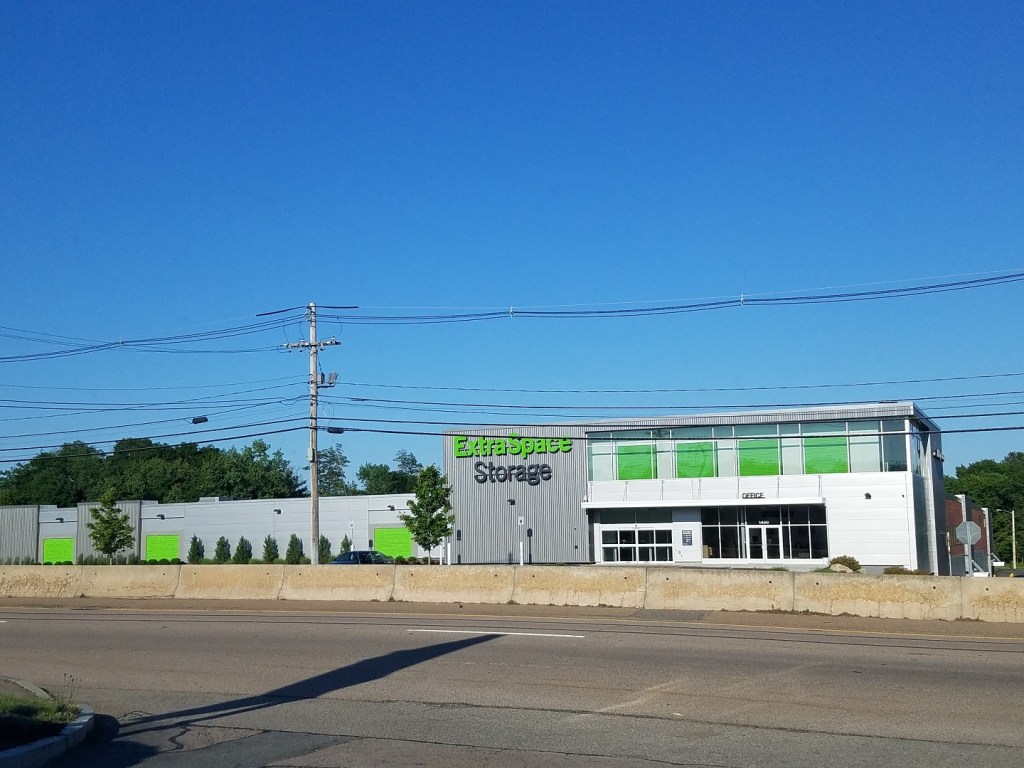 Exterior view of an Extra Space Storage facility, featuring a modern design with green accents, under a clear blue sky.