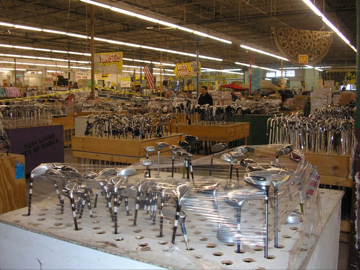 A large indoor market filled with various golf clubs on display, surrounded by miscellaneous merchandise and shoppers browsing.