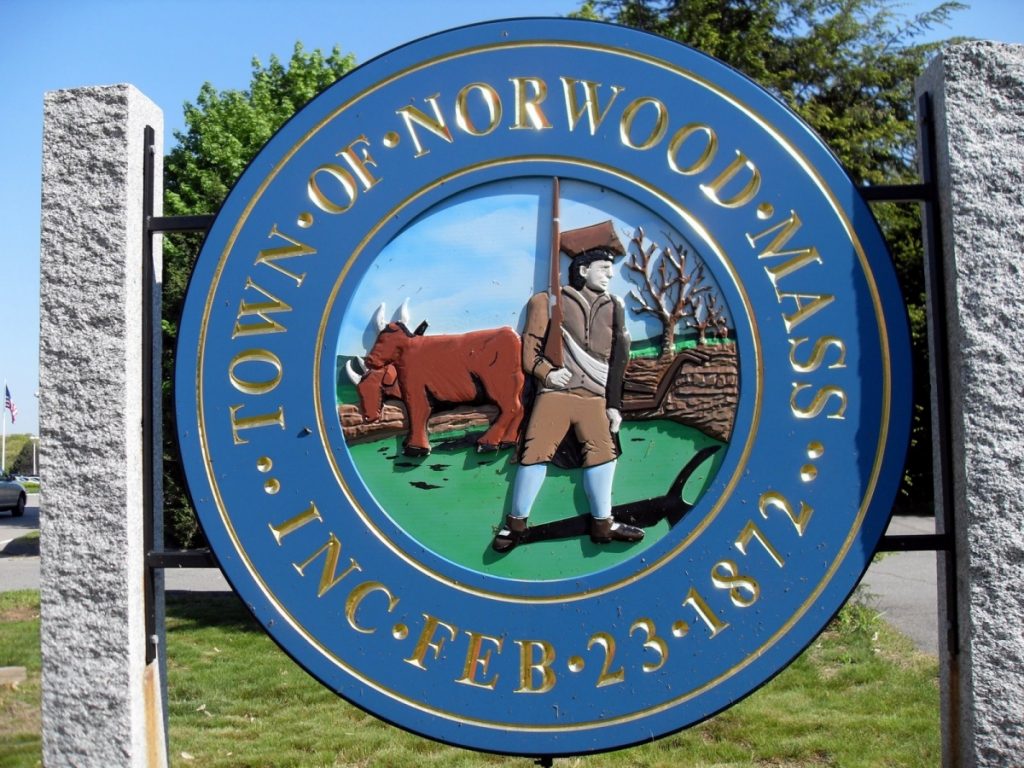 Town seal of Norwood, Massachusetts, featuring a man with a rifle and a cow in a pastoral setting, established February 23, 1872.