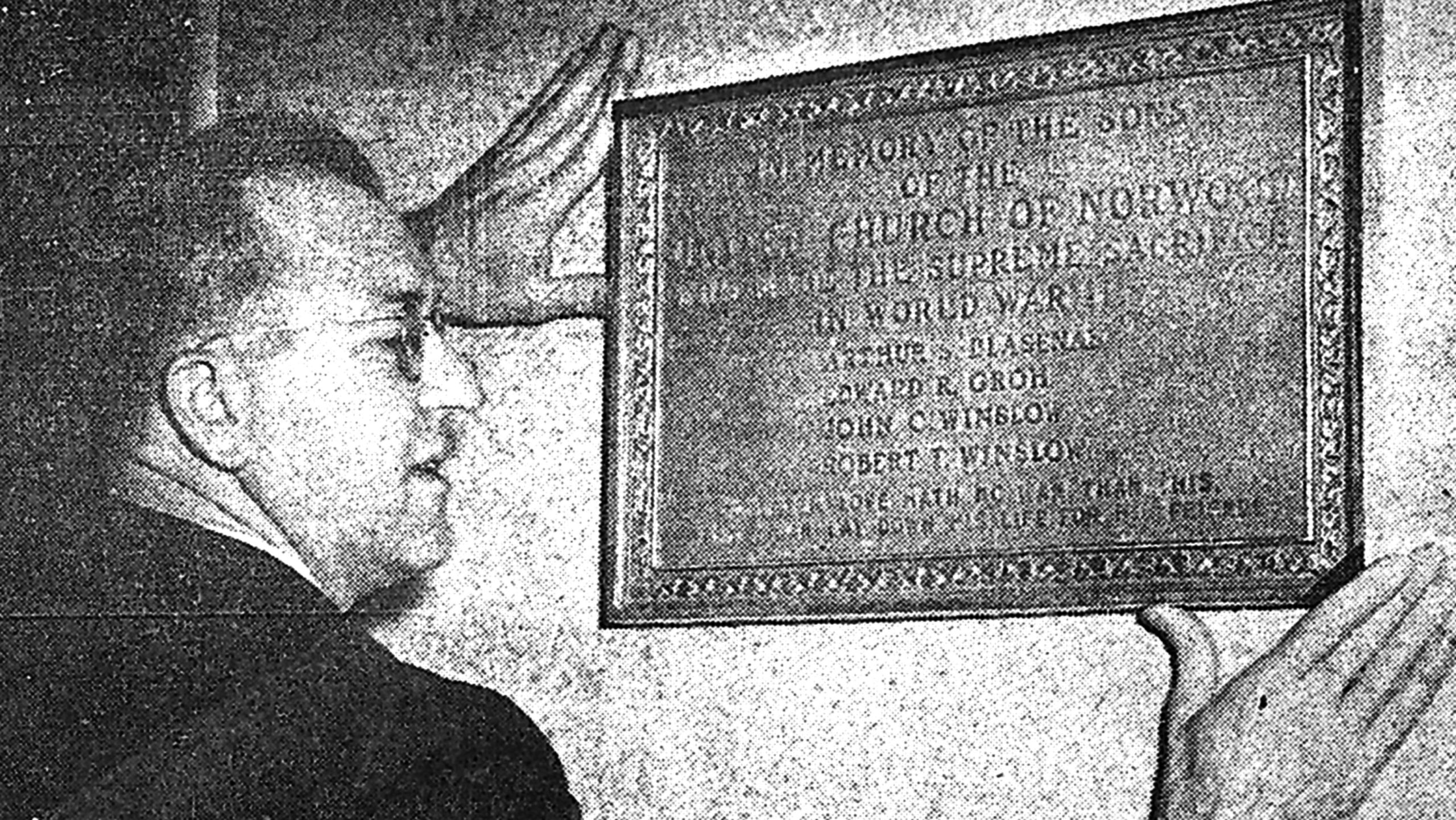 Rev. Edmund A. Miller, pastor, places the plaque dedicated Sunday at the United Church in honor of the sons of the church who made the supreme sacrifice in World War II (Surette Photo