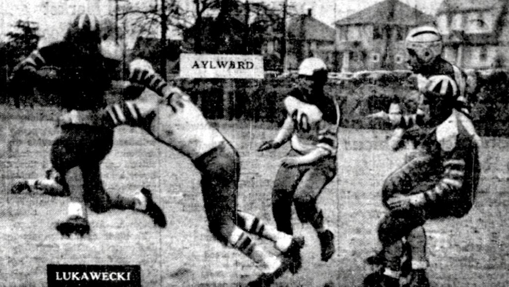 WHOA!—Bill Lukawecki, whirling Norwood High back, comes to the end of a 20-yard kick runback in the arms of Capt. Al Aylward, Dedham. Game ended in scoreless tie, with Dedham missing touchdown on last play of the contest.
