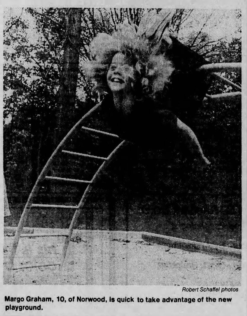 A young girl joyfully swinging on a playground apparatus with trees in the background.