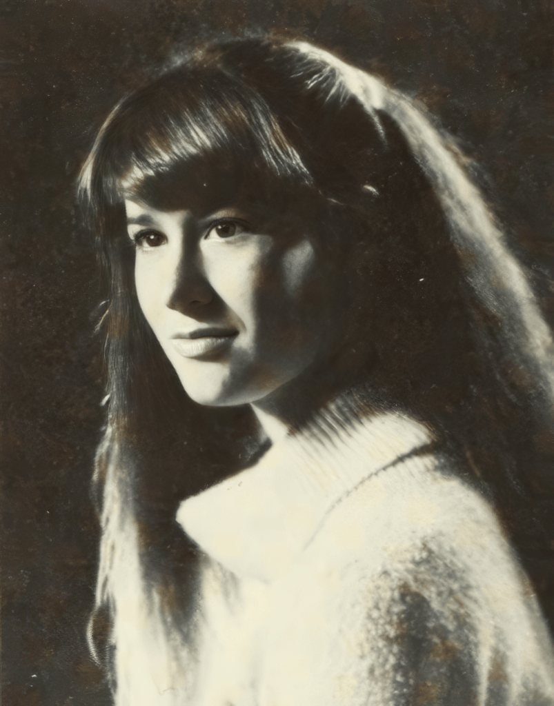 A black and white portrait of a young woman with long hair, wearing a high-necked sweater. She is gazing thoughtfully to the side.